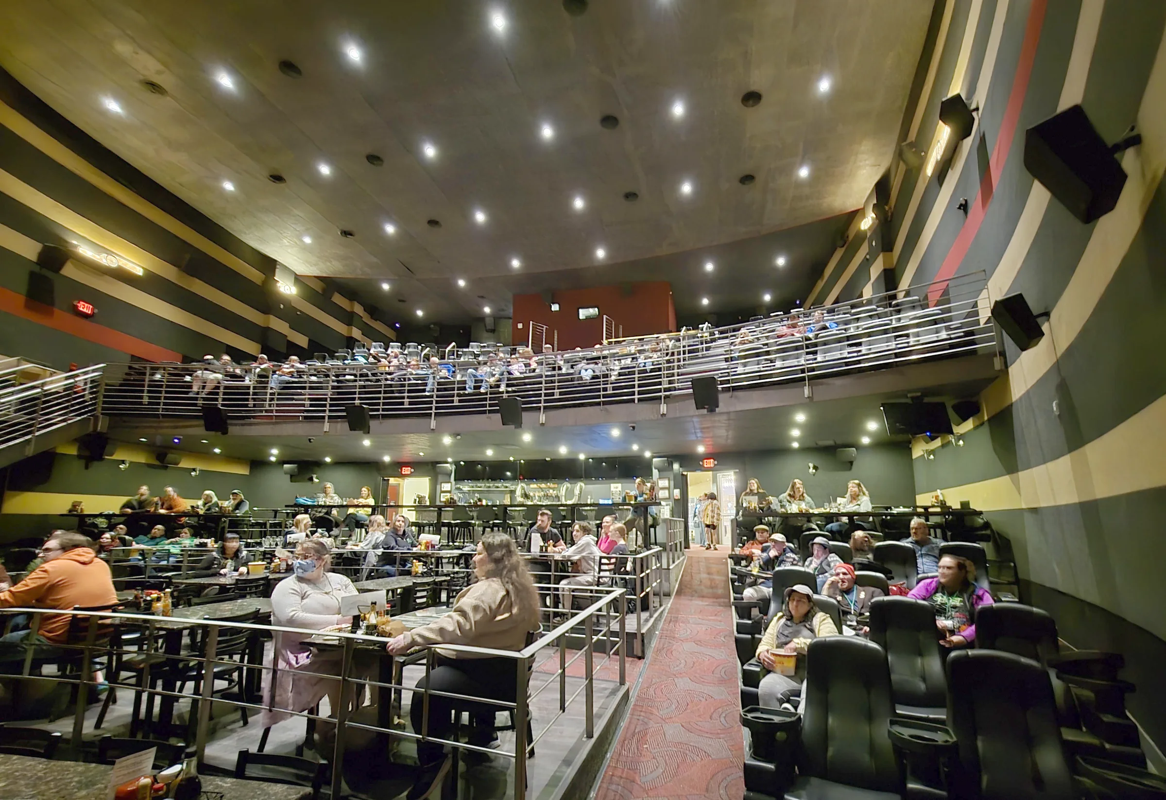 A packed theatre venue, audience filling the balcony and the floor tables below